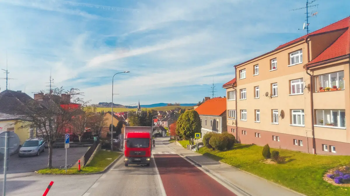 Červený kamion nákladní dopravy projíždí českou obcí po hlavní silnici
