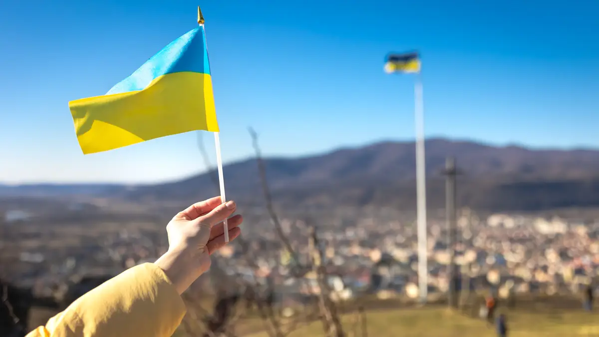 Ruka drží malou ukrajinskou vlajku nad městem v podhůří